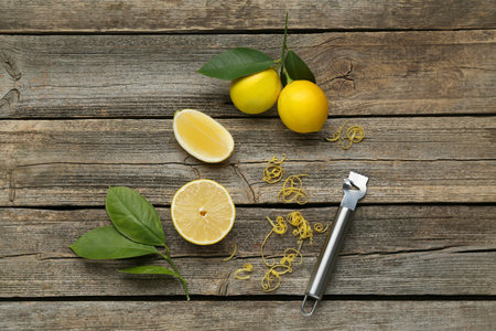 Lemon zest, zester tool and fresh fruits on wooden table, flat lay