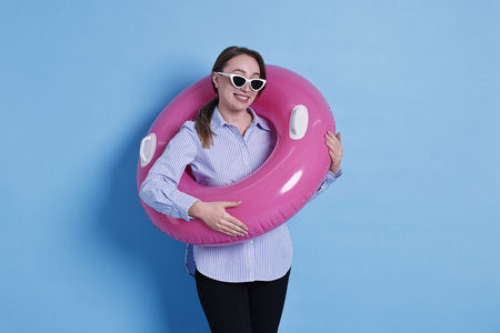 Businesswoman with inflatable ring and sunglasses on light blue background