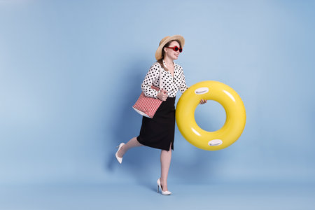 Businesswoman with inflatable ring, straw hat, bag and sunglasses on light blue backgroundの写真素材