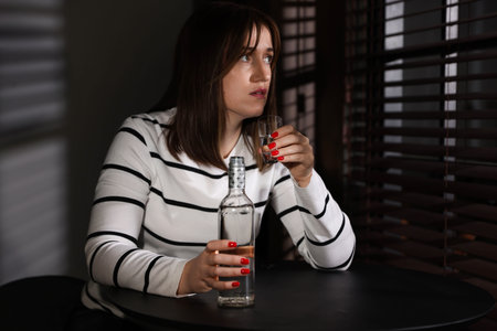 Woman with shot glass and bottle at table indoors