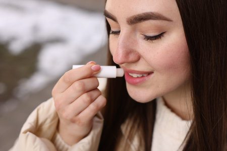 Beautiful young woman applying lip balm outdoors