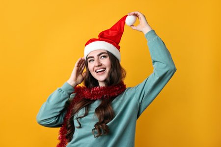Happy young woman with tinsel and Santa hat on orange backgroundの写真素材