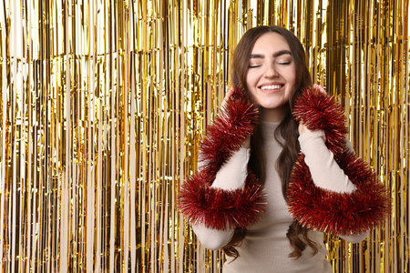 Happy young woman with tinsel against golden foil curtain. Space for textの写真素材