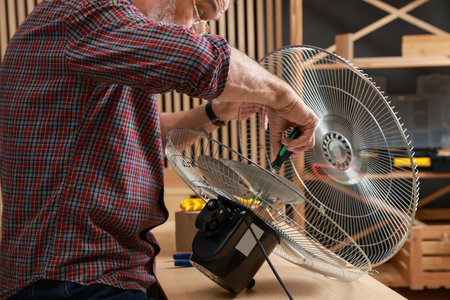 Relaxing hobby. Senior man repairing fan with screwdriver in workshop, closeup