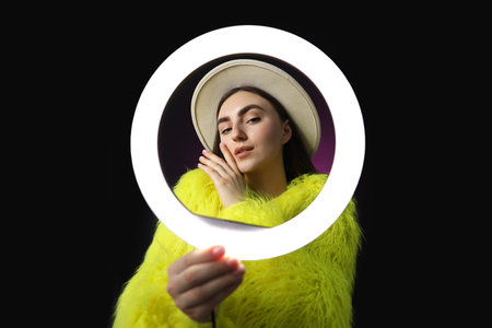 Stylish woman on dark purple background, view through ring lamp