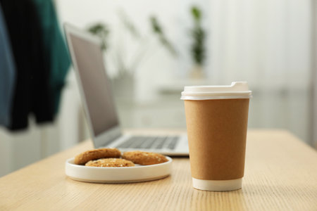 Paper cup, plate with cookies and laptop on wooden table indoors, closeup. Mockup for designの写真素材