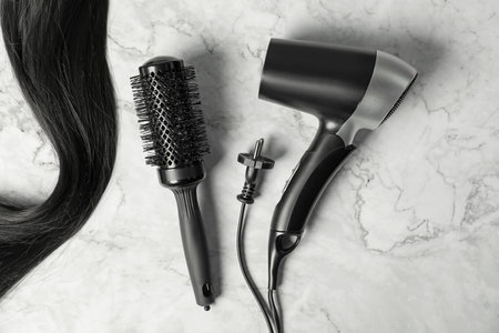 Stylish round brush, hairdryer and lock of black hair on white marble table, flat layの写真素材