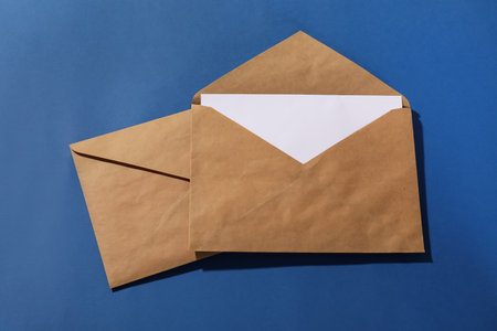 Kraft paper envelopes with letter on blue background, top view. Mockup for designの写真素材