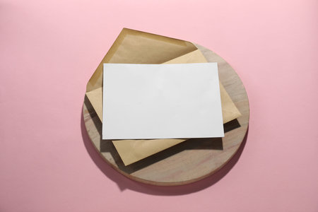 Kraft paper envelope with letter on pink background, above view. Mockup for design