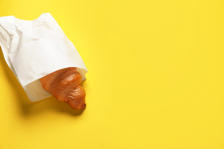 Paper bag with fresh croissant on yellow background, top view. Space for textの写真素材