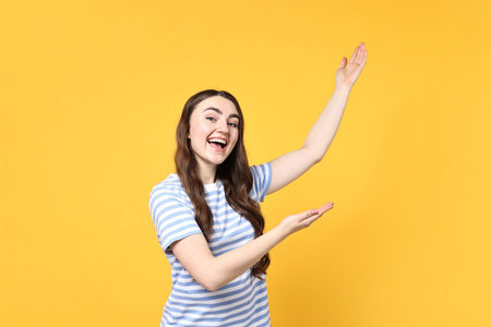 Happy woman welcoming friends or guests on yellow backgroundの写真素材