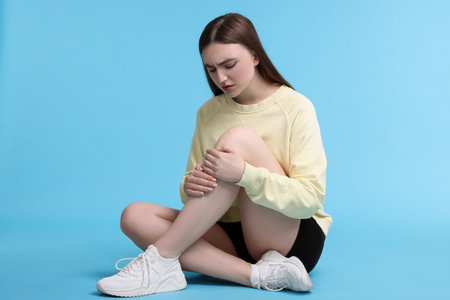 Young woman suffering from pain in knee on light blue backgroundの写真素材