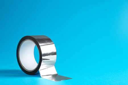 Roll of silver adhesive tape on light blue background, space for textの写真素材