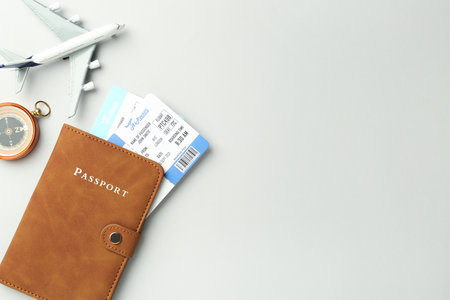 Passport in brown cover, plane model, compass and flight tickets on light grey background, flat lay. Space for textの写真素材