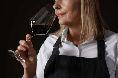 Professional sommelier tasting red wine in glass on black background, closeupの写真素材