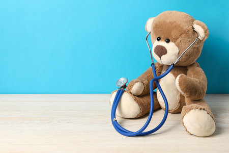 Pediatrics concept. Teddy bear with stethoscope on wooden table against light blue background, space for textの写真素材