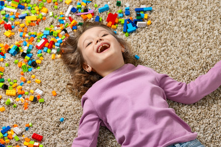 Cute girl lying near building blocks on carpet at homeの写真素材