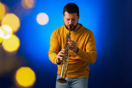 Professional musician playing soprano saxophone on blue background with blurred lights. Bokeh effectの写真素材