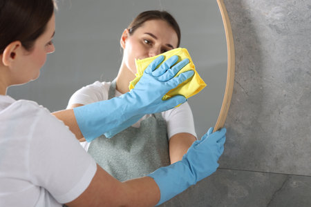 Woman cleaning mirror with rag indoors, space for text
