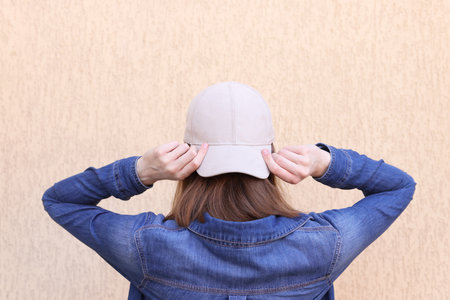 Woman in stylish baseball cap near beige wall, back view. Mockup for designの写真素材