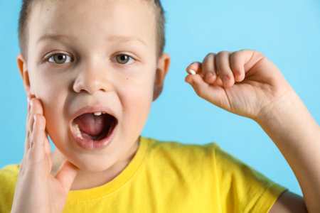 Cute little boy with missing tooth on light blue background, closeup. Waiting for tooth fairyの写真素材