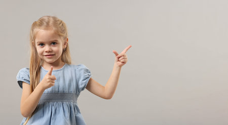 Cute little girl pointing at something on gray background. Space for textの写真素材