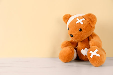 Teddy bear with bandages and sticking plasters on white marble table against beige background, space for textの写真素材