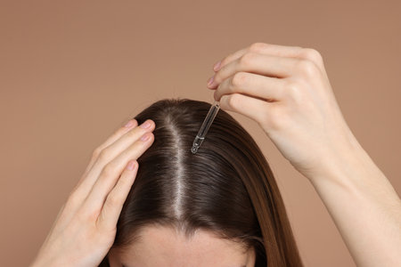 Hair loss problem. Girl applying serum onto hairline on dark beige background, closeupの写真素材