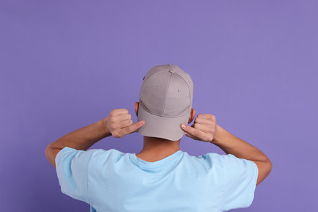 Man in stylish baseball cap on violet background, back view. Mockup for designの写真素材