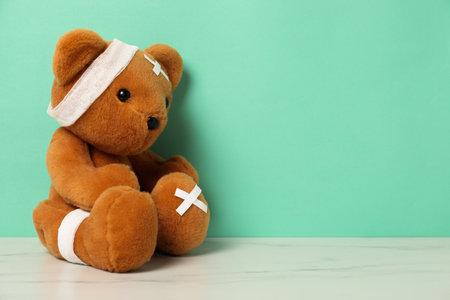 Teddy bear with bandages and sticking plasters on white marble table against turquoise background, space for textの写真素材