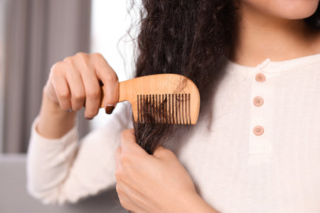 Woman brushing her curly hair with comb indoors, closeupの写真素材