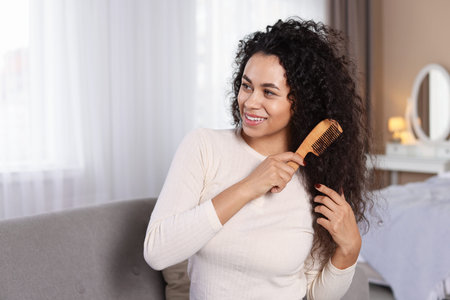 Smiling young woman brushing her curly hair with comb at homeの写真素材