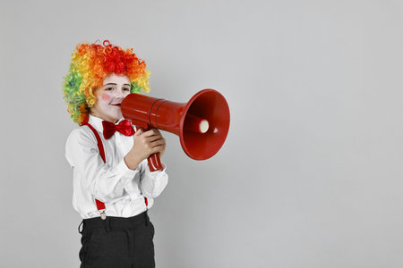 Little boy dressed like clown with megaphone on grey background, space for text. Surprise party