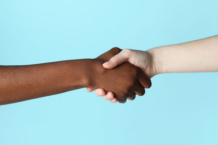 Stop racism. People of different skin colors shaking hands on light blue background, closeupの写真素材