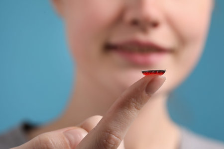 Woman with red color contact lens on light blue background, closeup. Selective focus