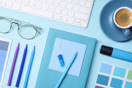 Designer's workplace. Flat lay composition with stationery and keyboard on light blue background