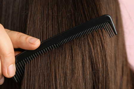 Woman brushing hair with plastic comb on pink background, closeup