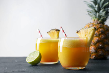 Tasty pineapple cocktail in glasses served on black table
