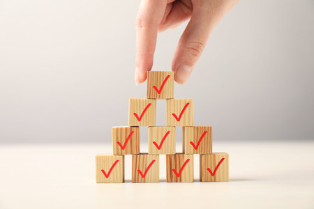 Woman building pyramid of wooden cubes with check marks at table, closeup