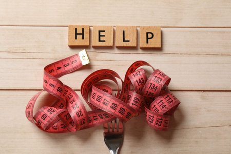 Bulimia. Word Help and fork with measuring tape on white wooden table, top view