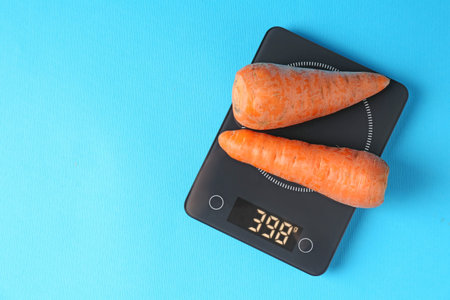 Electronic kitchen scale with carrots on light blue background, top view. Space for textの写真素材