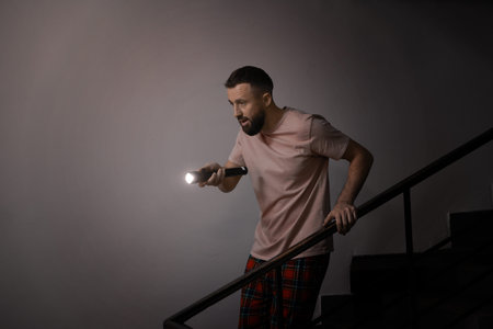 Fear of darkness. Scared man with flashlight indoors at nightの写真素材