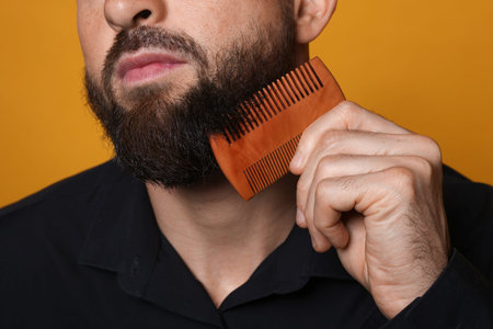 Man combing beard on orange background, closeup