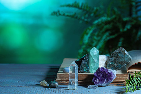 Beautiful natural gemstones and book on grey table against green background. Space for text