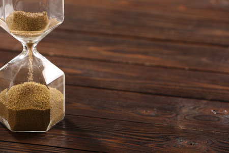 Hourglass with flowing sand on wooden table, closeup. Space for text