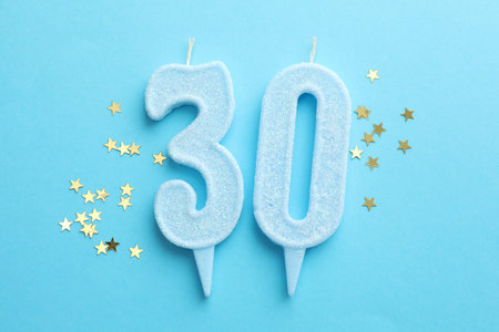30th birthday. Number shaped candles and confetti on light blue background, flat lay