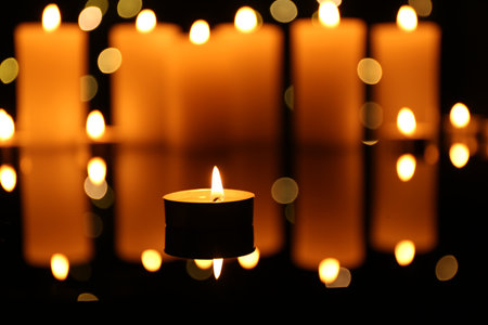 Burning candles on mirror surface in darkness, closeup. Bokeh effectの写真素材