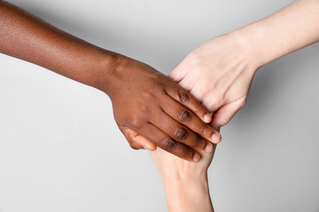 Stop racism. People of different skin colors joining hands on light grey background, closeup