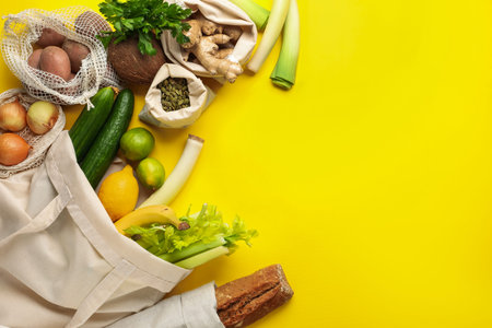 Eco bags with different food products on yellow background, flat lay. Space for text