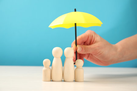 Woman holding umbrella over human figures at white table, closeup. Insurance conceptの写真素材